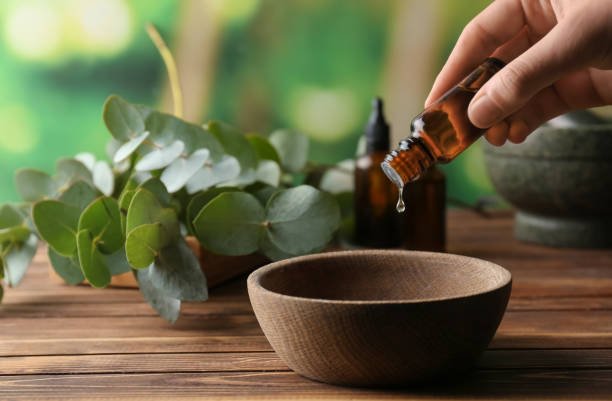 Home woman pouring eucalyptus essential oil into bowl on wooden table