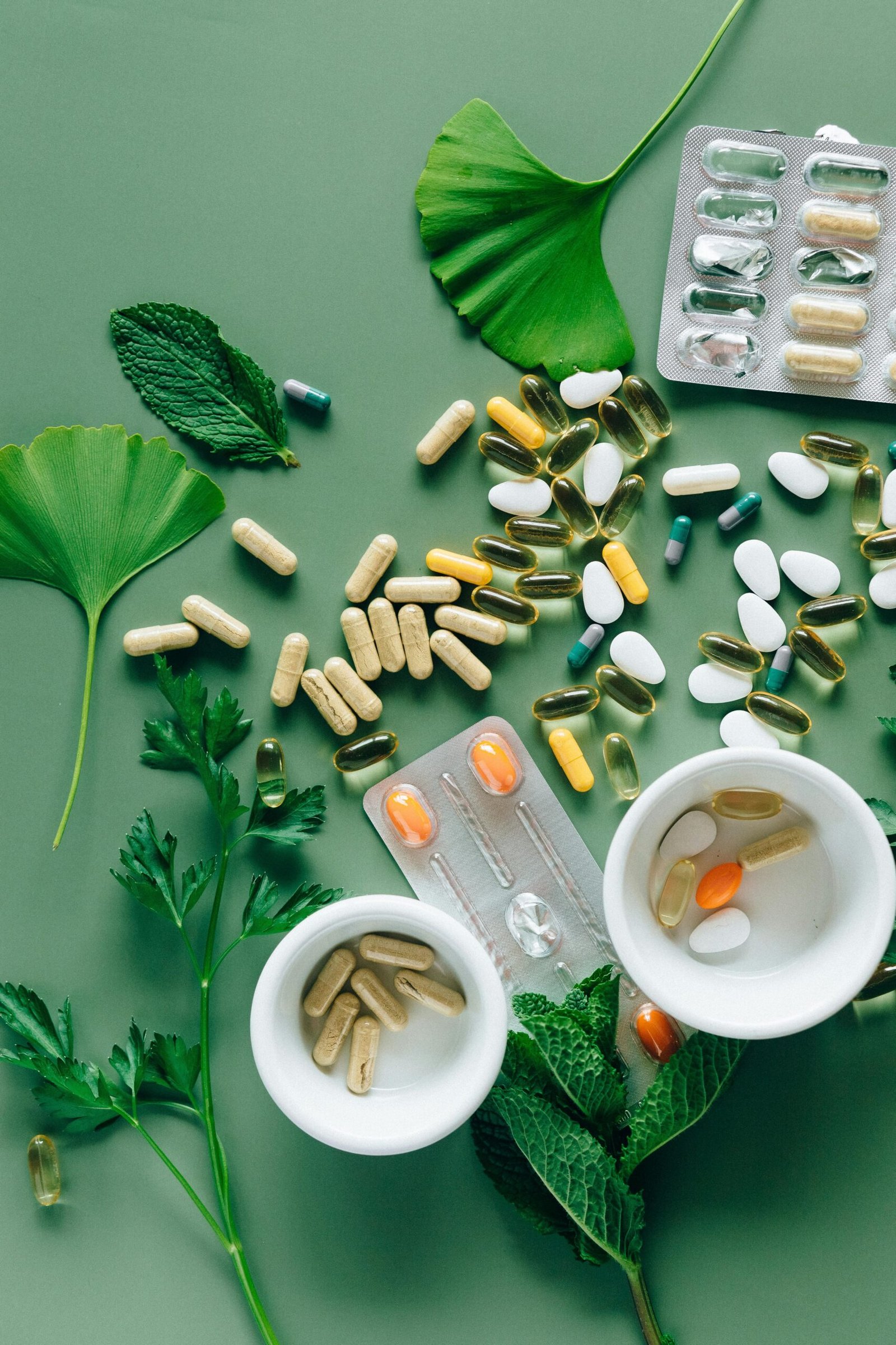Home Flat lay of assorted pills and herbs on green surface, symbolizing health and wellness.